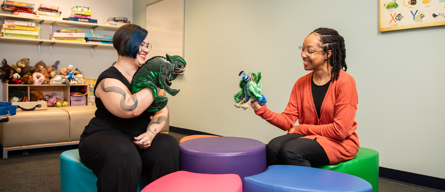 Play Therapy Two female students sitting across from each other smiling with puppets on their hands