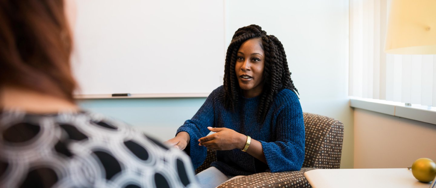 _0004_Advising Information.jpg A woman seated in an arm chair gesturing with her hands, facing another person.