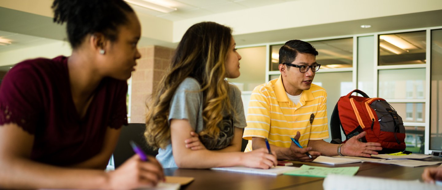 Banner - Curriculum Two students sitting at a table look at a third who is speaking