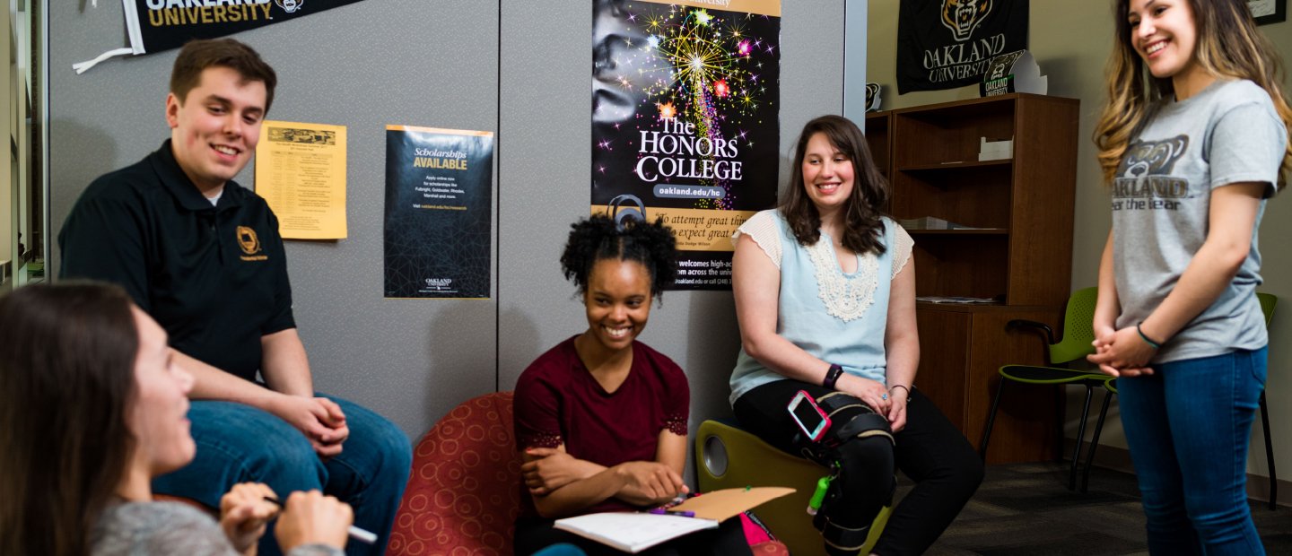 Banner - For Students A group of young people sits in an office, talking and laughing. An Honors College poster can be seen in the background.