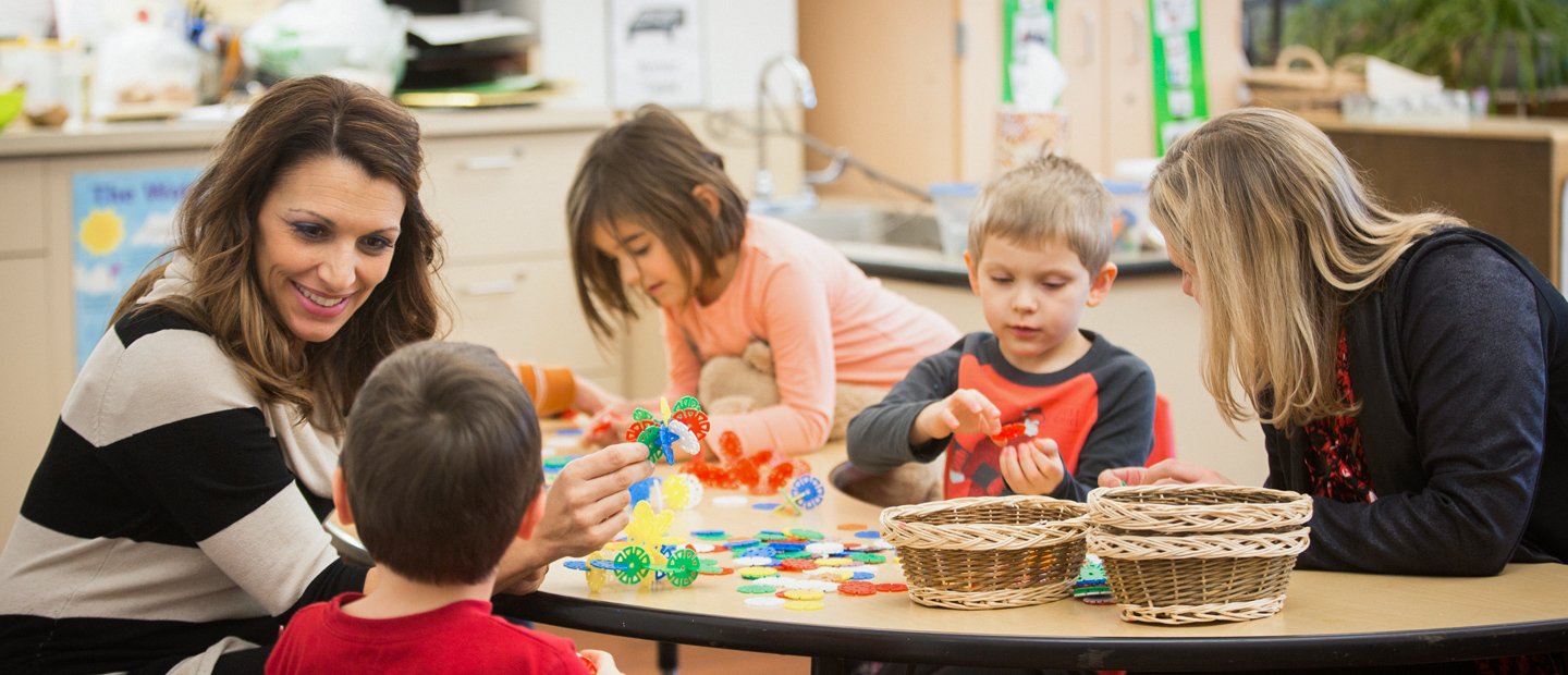 _0001_special-education_med-in-special-education.jpg Two women sitting at a table with 3 children