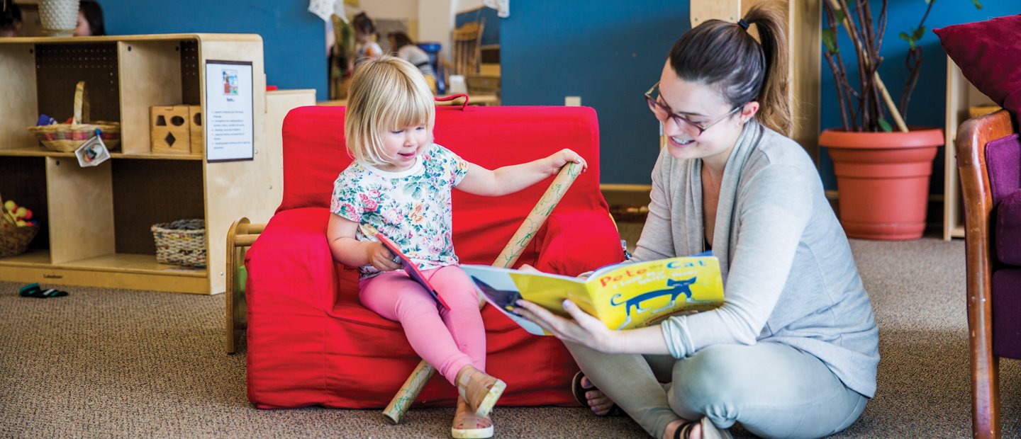 _0009_early-childhood-education_ece.jpg Woman reading book to child sitting on a chair