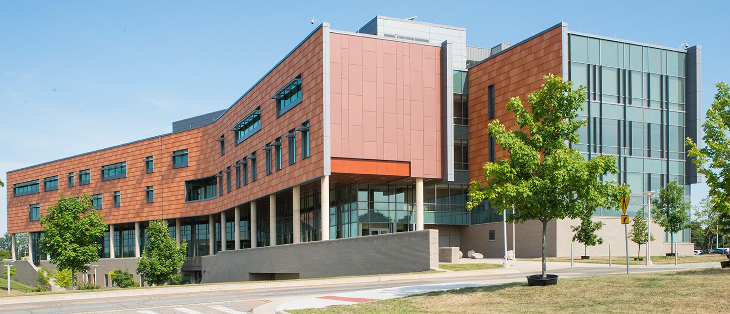 SON-19888_about.jpg exterior of a brick and glass building with green trees around it