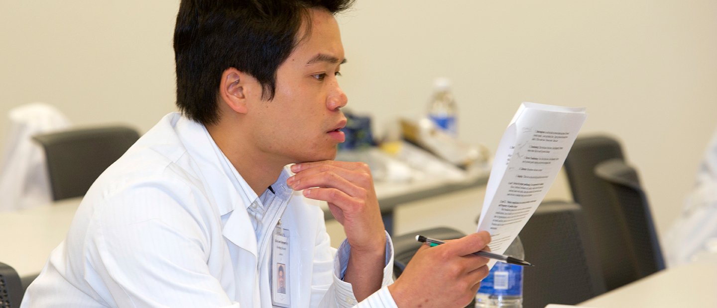 SON-19888_forms.jpg man in a white lab coat holding a pencil, looking over a form