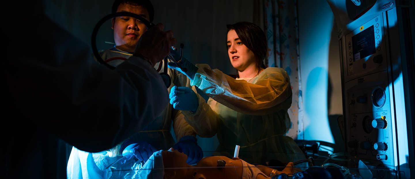 SON-19888_student-resources.jpg two students practicing with medical equipment in a dark room