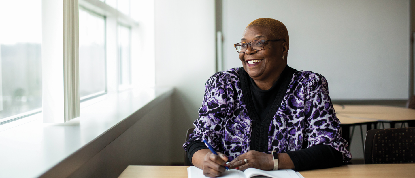 EdD_Banner.jpg Photo of an african american woman sitting at a desk smiling out the window next to her