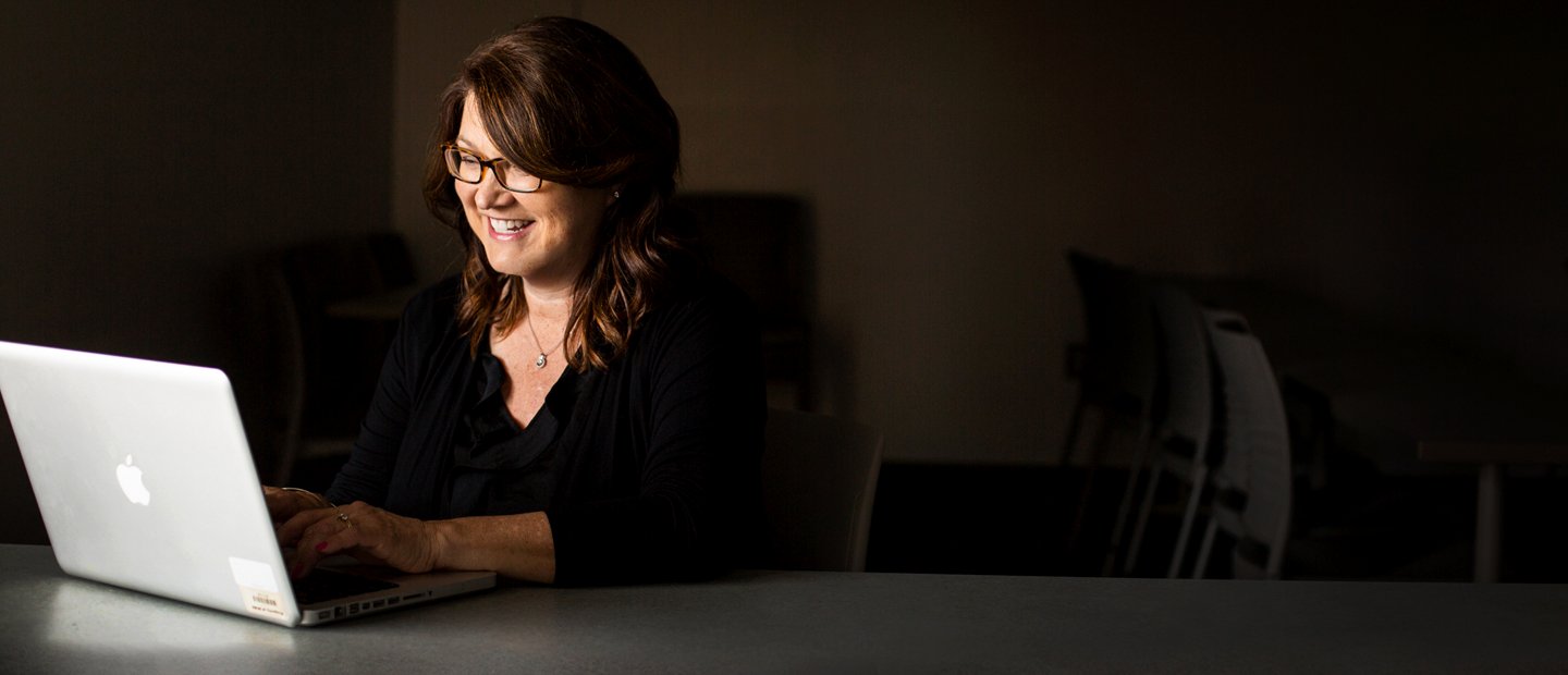 GI0A9964.jpg woman seated at a table with an open laptop in a dark room
