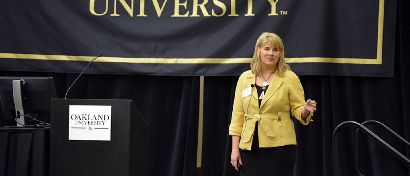 edleadership.jpg woman speaking on a stage with an Oakland University banner behind her