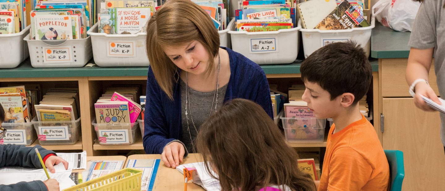 SFS Elementary Education.jpg teacher sitting with a few kids and helping them learn