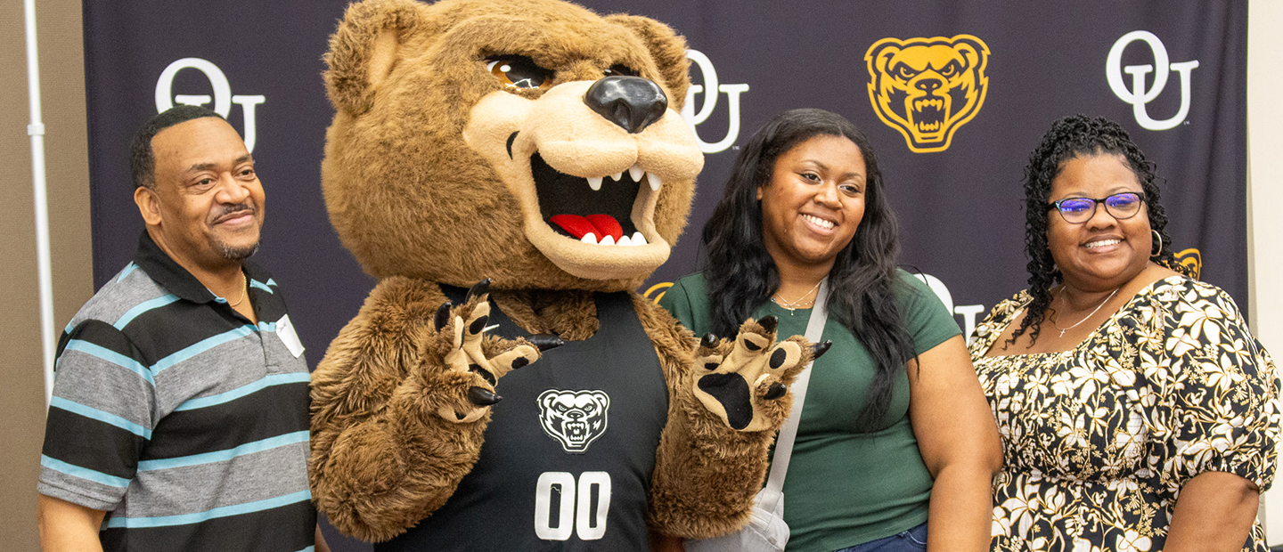 New Student Orientation FAQs A new Oakland University student and her parents posing with the Grizz mascot